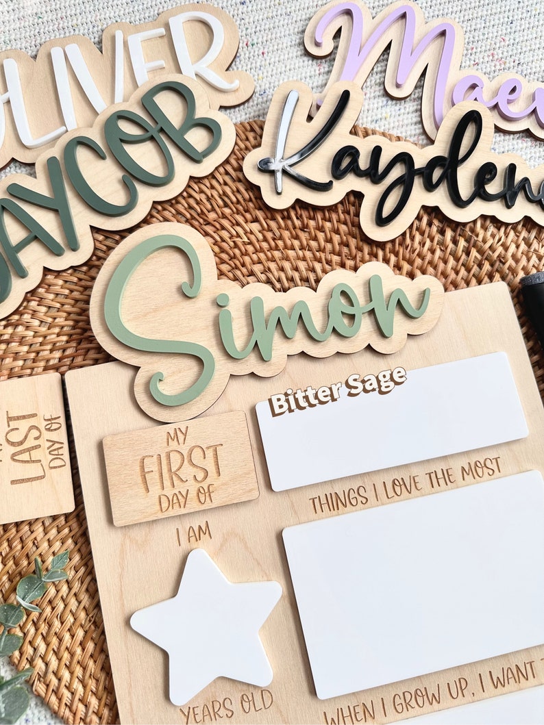 May include: A wooden milestone board featuring the text My First Day Of, I Am, Years Old, Things I Love The Most, and When I Grow Up, I Want To. The board includes a white star shape and blank white rectangular areas for writing with markers.
