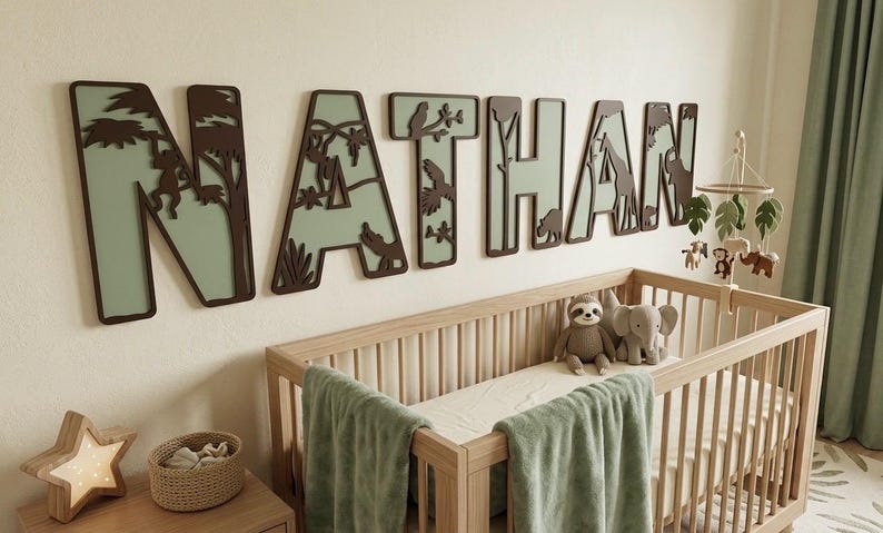 Op de afbeelding: Een kinderkamersc&egrave;ne met een houten wieg, een groene deken en knuffels. Boven de wieg staat de naam "NATHAN" in grote, decoratieve letters met een junglethema, inclusief dieren en bladeren.