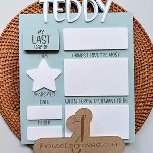 Puede incluir: Un letrero de madera azul claro con letras blancas que dice "My Last Day Of". Hay espacios en blanco para completar informaci&oacute;n sobre la persona, como su edad, altura y lo que quiere ser cuando sea mayor. El letrero tambi&eacute;n tiene una forma de estrella y el texto "Teddy" en la parte superior.