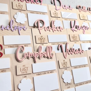K&ouml;nnte beinhalten: Ein Satz aus Holztafeln mit personalisierten Namen und Platz zum Ausf&uuml;llen von Details &uuml;ber den ersten und letzten Tag einer Person. Die Tafeln sind mit rosa, lila und roten Buchstaben verziert. Der Text auf den Tafeln lautet "Mein erster Tag", "Mein letzter Tag", "Die Dinge, die ich am meisten liebe", "Jahre alt", "Datum", "Gr&ouml;&szlig;e", "Wenn ich gro&szlig; bin, m&ouml;chte ich sein", und "Die Dinge, die ich am meisten liebe".