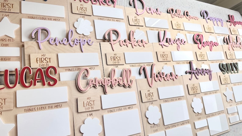 K&ouml;nnte beinhalten: Ein Satz aus Holztafeln mit personalisierten Namen und Platz zum Ausf&uuml;llen von Details &uuml;ber den ersten und letzten Tag einer Person. Die Tafeln sind mit rosa, lila und roten Buchstaben verziert. Der Text auf den Tafeln lautet "Mein erster Tag", "Mein letzter Tag", "Die Dinge, die ich am meisten liebe", "Jahre alt", "Datum", "Gr&ouml;&szlig;e", "Wenn ich gro&szlig; bin, m&ouml;chte ich sein", und "Die Dinge, die ich am meisten liebe".