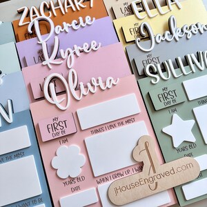 Puede incluir: Un conjunto de placas de madera personalizadas con los nombres Zachary, Darcie, Kyree, Olivia, Ella, Jackson y Sullivan. Cada placa tiene un espacio para la informaci&oacute;n del primer d&iacute;a de escuela de un ni&ntilde;o, incluyendo su edad, fecha y las cosas que m&aacute;s le gustan. Las placas est&aacute;n pintadas en varios colores pastel, incluyendo rosa, azul, verde y amarillo.