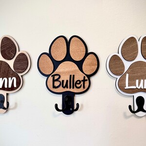 May include: Three wooden paw print hooks with double hooks, each with a different dog's name: Finn, Bullet, and Luna.