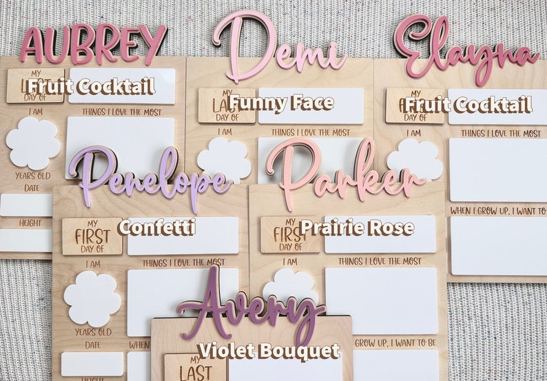 K&ouml;nnte beinhalten: Ein Satz von acht personalisierten Holz-Wachstumstabellen mit rosa, lila und wei&szlig;en Akzenten. Jede Tabelle zeigt den Namen eines Kindes, ein einzigartiges Thema und Platz zum Aufzeichnen von Meilensteinen wie Gr&ouml;&szlig;e, Alter und Lieblingsdingen.