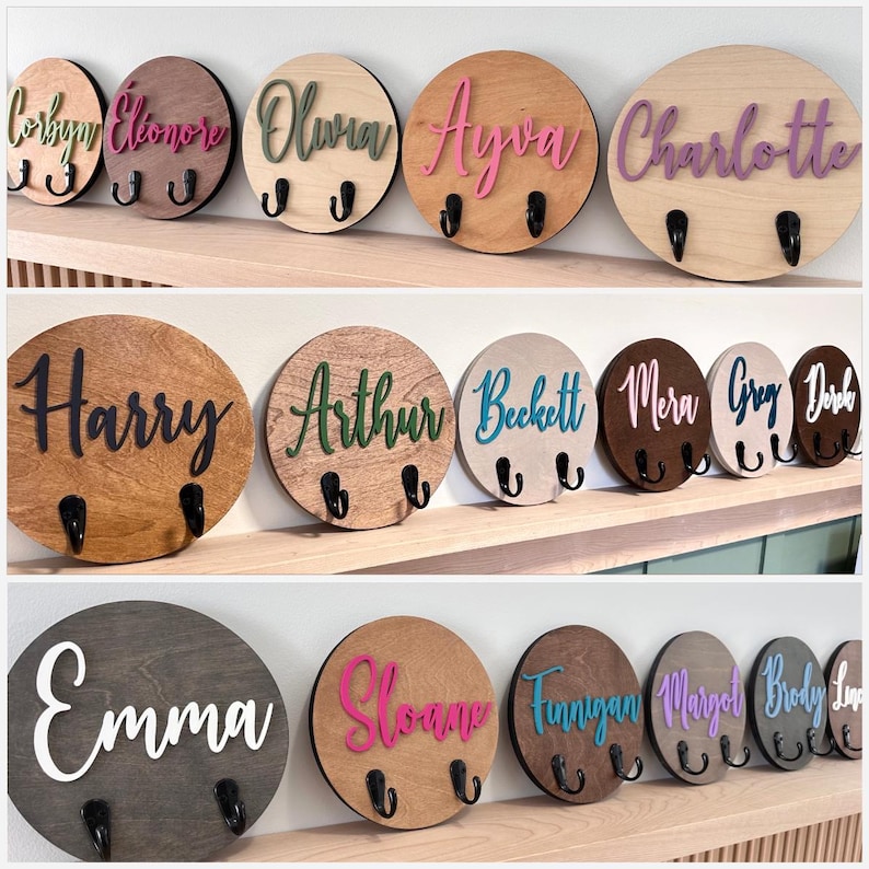 Puede incluir: Una colecci&oacute;n de ganchos de pared circulares de madera con varios nombres en letras cursivas coloridas y en relieve. Cada placa redonda est&aacute; hecha de madera en diferentes tonos e incluye dos ganchos de metal negro.