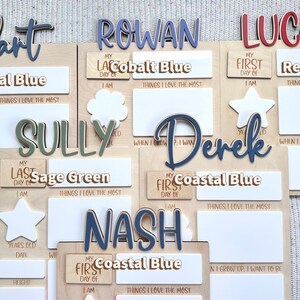 K&ouml;nnte beinhalten: Holzschildchen mit personalisierten Namen wie Hart, Rowan, Lucas, Sully, Derek und Nash. Jedes Schildchen hat Platz f&uuml;r den ersten oder letzten Schultag eines Kindes, sein Alter, Datum, Gr&ouml;&szlig;e und die Dinge, die es am meisten liebt. Die Schildchen sind in verschiedenen Farben bemalt, darunter Blau, Gr&uuml;n und Rot.