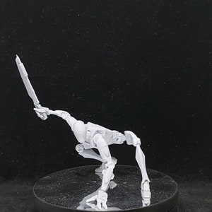 May include: A light gray articulated action figure in a dynamic pose, holding a sword. The figure is crouched low, with one leg extended and the other bent. The sword is held high, suggesting action. The figure is on a black surface.