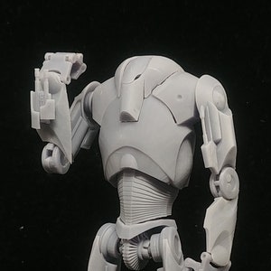 Peut inclure: Une figurine d'action en plastique gris d'un robot avec des membres articulés. Le robot a un design détaillé avec une surface texturée.