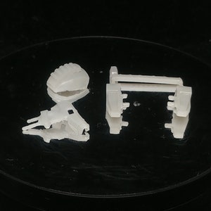 May include: A collection of small, off-white plastic components, possibly for a larger device, are arranged on a black surface. The pieces include a rectangular frame, a curved piece, and a complex, angled structure.