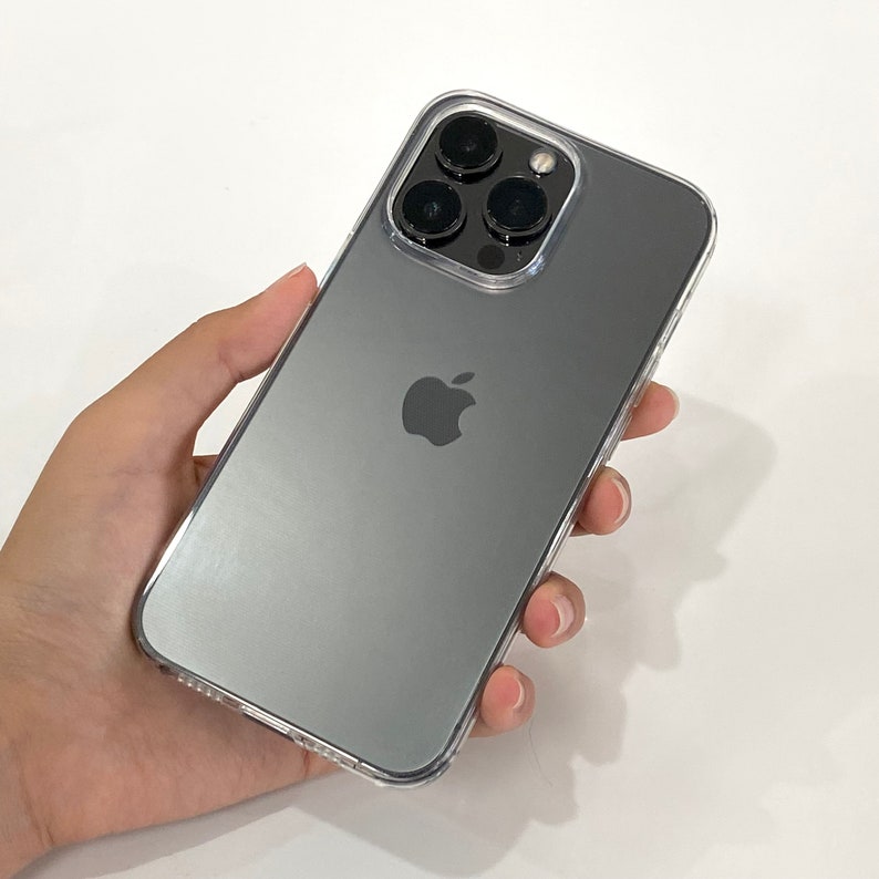 Pu&ograve; includere: Un iPhone nero con una custodia trasparente. Il telefono ha un logo Apple argentato e un gruppo di fotocamere con quattro obiettivi.