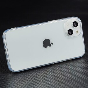 Pu&ograve; includere: Una custodia per telefono trasparente con un telefono bianco all'interno. Il telefono ha un logo Apple nero sul retro e un obiettivo della fotocamera con due cerchi neri.