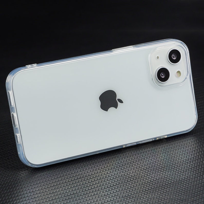 Pu&ograve; includere: Una custodia per telefono trasparente con un telefono bianco all'interno. Il telefono ha un logo Apple nero sul retro e un obiettivo della fotocamera con due cerchi neri.