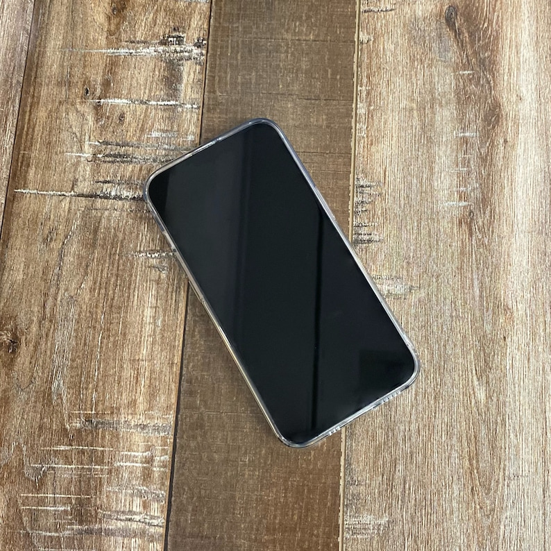Pu&ograve; includere: Uno smartphone nero con uno schermo scuro &egrave; appoggiato su una superficie di legno.