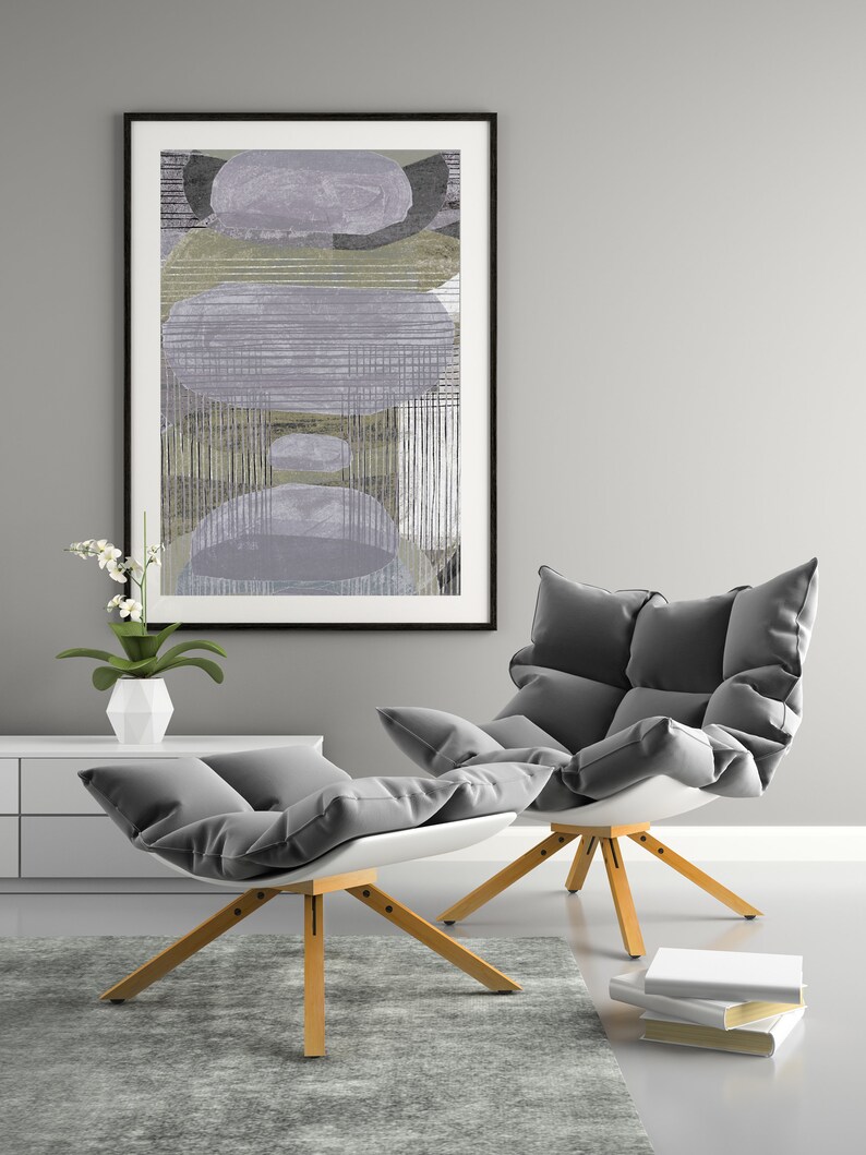 May include: Two gray cushioned chairs with wooden legs, one with a white footrest, in front of a gray wall with a framed abstract painting.