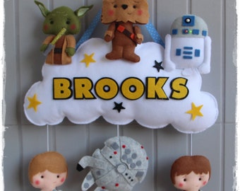 May include: A white felt cloud with the name "BROOKS" in yellow felt letters. The cloud is decorated with yellow stars and has five felt characters hanging from it: Yoda, Chewbacca, R2-D2, a TIE fighter, and Luke Skywalker.