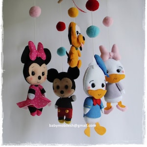 Pode incluir: Móbile de bebê feito à mão com personagens da Disney em feltro, incluindo Mickey e Minnie Mouse, Pato Donald e Margarida, e Pluto. O móbile tem uma estrutura de madeira com bolas de feltro penduradas em várias cores. O endereço de e-mail babymobilesh@gmail.com é visível.