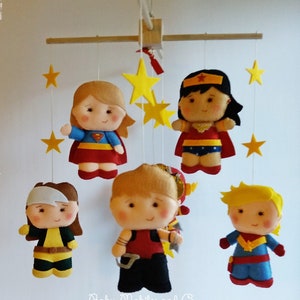 May include: A baby mobile with six felt superhero characters, including Wonder Woman, Superman, Captain Marvel, and others. The mobile is suspended from a wooden dowel rod and features yellow felt stars.
