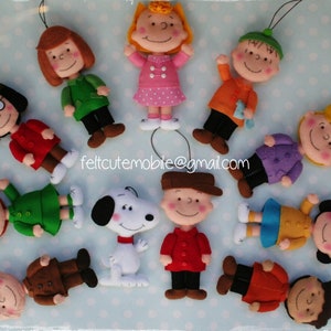 Op de afbeelding: Een verzameling Peanuts-figuren van vilt, waaronder Charlie Brown, Lucy, Snoopy en Linus. De figuren zijn allemaal handgemaakt en hebben verschillende gezichtsuitdrukkingen. De figuren dragen allemaal verschillende outfits, waaronder een rood shirt, een groen shirt, een blauw shirt en een geel shirt. De figuren staan allemaal op een blauwe achtergrond.