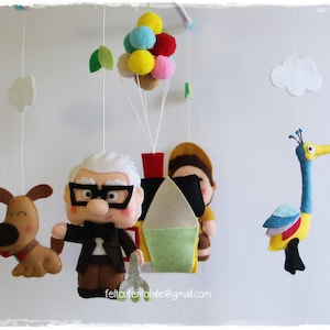 Pode incluir: Um m&oacute;bile de feltro para beb&ecirc; com uma casa, um cachorro, um p&aacute;ssaro e dois personagens do filme Up. A casa est&aacute; presa a um grupo de bal&otilde;es coloridos. O m&oacute;bile est&aacute; pendurado em um teto branco.