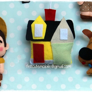 Op de afbeelding: Vilt speelgoedmobiel met een huis, een jongensscout, een hond en de tekst "feltcutemobile@gmail.com".