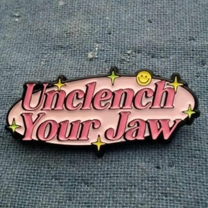 Unclench Your Jaw enamel pin 1.5 inch by 0.5 inch