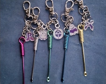 May include: Five metal keychains featuring long, thin stems with coiled tops and small scoops at the bottom. Each keychain includes a silver lobster clasp and a unique acrylic charm in purple and white, showcasing various geometric and graphic symbols.