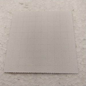 K&ouml;nnte beinhalten: Ein wei&szlig;es quadratisches Blatt Papier mit einem Rastermuster aus kleinen, gleichm&auml;&szlig;ig verteilten L&ouml;chern.