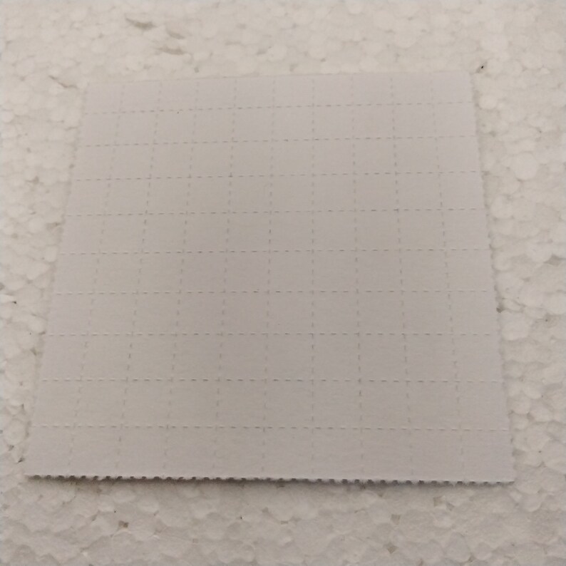 K&ouml;nnte beinhalten: Ein wei&szlig;es quadratisches Blatt Papier mit einem Rastermuster aus kleinen, gleichm&auml;&szlig;ig verteilten L&ouml;chern.