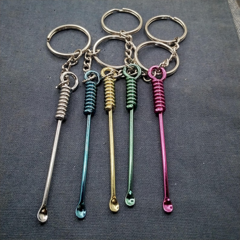 Puede incluir: Una colecci&oacute;n de llaveros con peque&ntilde;as herramientas met&aacute;licas de colores. Cada herramienta tiene un lazo para el llavero, una secci&oacute;n en espiral y una peque&ntilde;a cuchara redondeada en el extremo. Los colores incluyen plata, azul, oro, verde y rosa.