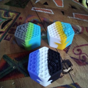 Pu&ograve; includere: Tre contenitori esagonali in silicone con un motivo a nido d'ape e un designo di ape. I contenitori sono blu, gialli e neri con accenti bianchi.