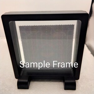 K&ouml;nnte beinhalten: Schwarzer Pr&auml;sentationsrahmen mit einer klaren Glasfront und einem schwarzen St&auml;nder. Der Rahmen ist leer und tr&auml;gt den Text "Sample Frame" auf der Vorderseite.