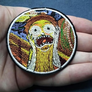 May include: Embroidered patch featuring a cartoon character with a wide open mouth and hands on its face. The patch has a black border and a white background. The character's face is yellow, brown, and white, with a background of blue, green, and brown.