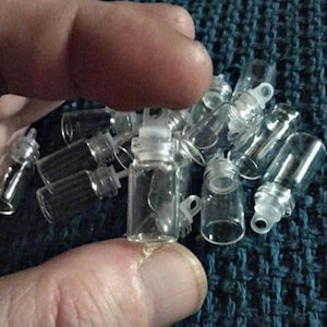 May include: A collection of small, clear glass vials with white plastic stoppers. The vials are cylindrical and appear to be empty. The stoppers have a small loop. The vials are scattered on a blue textured surface.