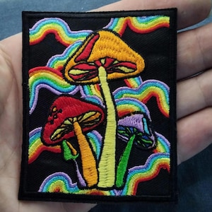 May include: Embroidered patch featuring colorful mushrooms with rainbow accents on a black background. The patch showcases a vibrant design with red, yellow, and purple mushroom caps, and a psychedelic aesthetic. Perfect for jackets, bags, or other fabric items.