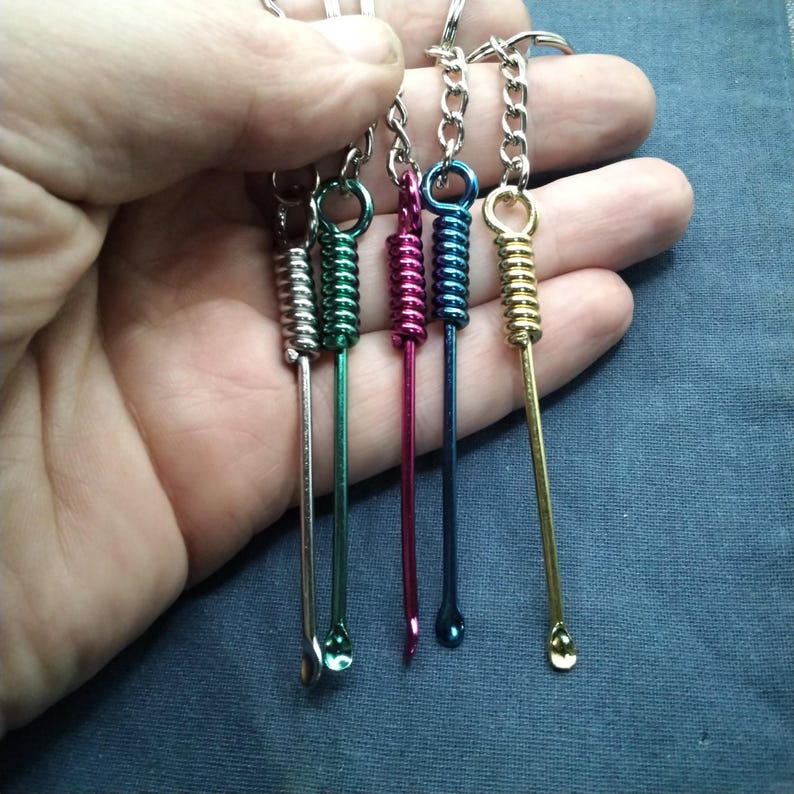 Puede incluir: Una colecci&oacute;n de llaveros coloridos con peque&ntilde;as herramientas de metal. Cada llavero tiene un color diferente, incluyendo plata, verde, rosa, azul y dorado. Las herramientas tienen un dise&ntilde;o de resorte y una peque&ntilde;a cuchara en el extremo.