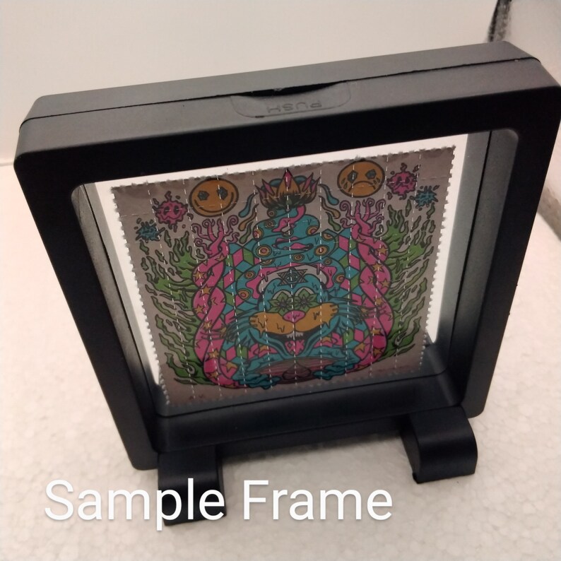 K&ouml;nnte beinhalten: Ein schwarzer Rahmen mit einer klaren Vorderseite und einem St&auml;nder unten. Der Rahmen enth&auml;lt einen farbenfrohen psychedelischen Kunstdruck mit einer Kreatur in der Mitte.