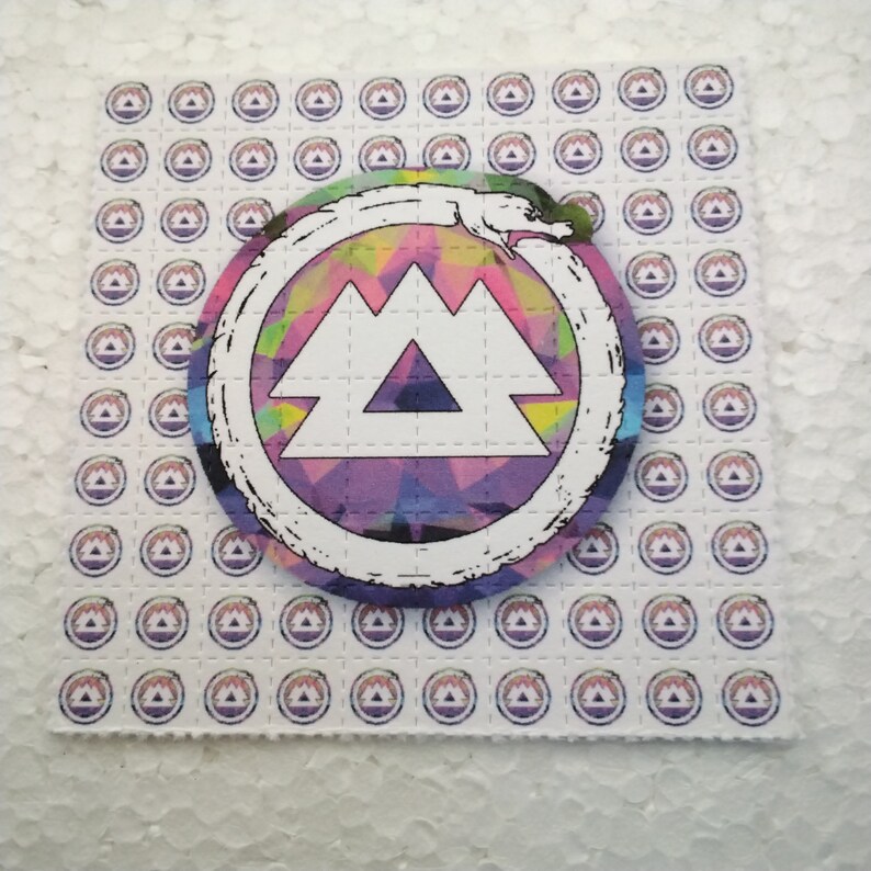 K&ouml;nnte beinhalten: Ein Blatt wei&szlig;es Papier mit einem sich wiederholenden Muster eines lila und wei&szlig;en Berglogos. Eine gr&ouml;&szlig;ere Version des Logos befindet sich in der Mitte des Blattes, mit einem farbenfrohen, abstrakten Design innerhalb des Berglogos. Das gr&ouml;&szlig;ere Logo ist von einem wei&szlig;en Kreis mit einem schwarzen Schlangendesign umgeben.