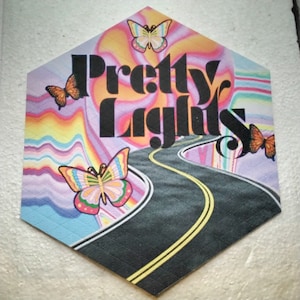 May include: A hexagonal sticker with a psychedelic design featuring a winding road, colorful butterflies, and the text "Pretty Lights".