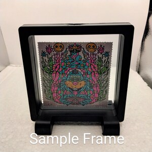 K&ouml;nnte beinhalten: Ein schwarzer Rahmen mit einer klaren Acrylglasscheibe zeigt einen farbenfrohen psychedelischen Kunstdruck. Der Druck zeigt eine Kreatur mit mehreren Augen und einer Krone. Der Druck ist von einem rosa und gr&uuml;nen Karomuster umgeben.