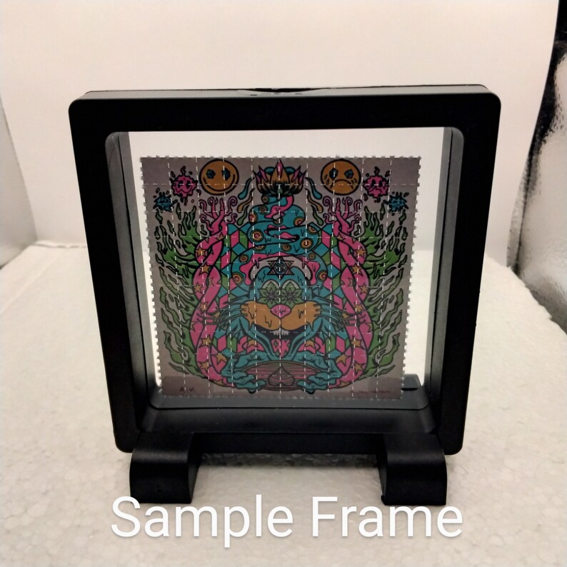 K&ouml;nnte beinhalten: Ein schwarzer Rahmen mit einer klaren Acrylglasscheibe zeigt einen farbenfrohen psychedelischen Kunstdruck. Der Druck zeigt eine Kreatur mit mehreren Augen und einer Krone. Der Druck ist von einem rosa und gr&uuml;nen Karomuster umgeben.