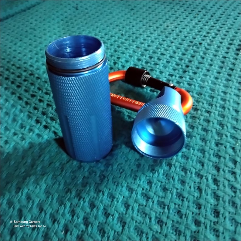 Shows a blue metal container, a cylindrical round, open-ended container. The cylindrical container has a textured surface and the lid has a textured rim.