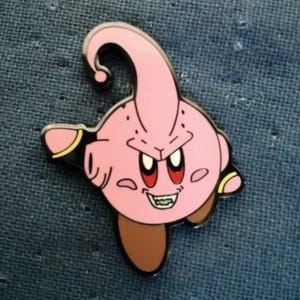 May include: A pink enamel pin featuring a cartoon character with a large, curved antenna, angry eyes, and a wide grin. The character has brown feet and black accents on its arms. The pin is set against a blue textured background.