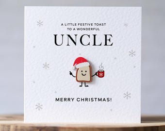 May include: A square white greeting card featuring the text A LITTLE FESTIVE TOAST TO A WONDERFUL UNCLE and MERRY CHRISTMAS! with a central illustration of a piece of toast wearing a Santa hat and holding a red mug with a snowflake.