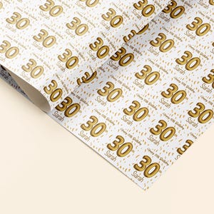 May include: White wrapping paper with a repeating pattern of gold 30th birthday balloons and confetti. The text "Happy 30th Birthday" and the name "Sarah" are repeated throughout the pattern.