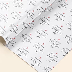 Op de afbeelding: Wit inpakpapier met een herhalend patroon van roze harten en de tekst "Happy 21st Birthday Twenty One Zoe" in zwarte cursieve letters.