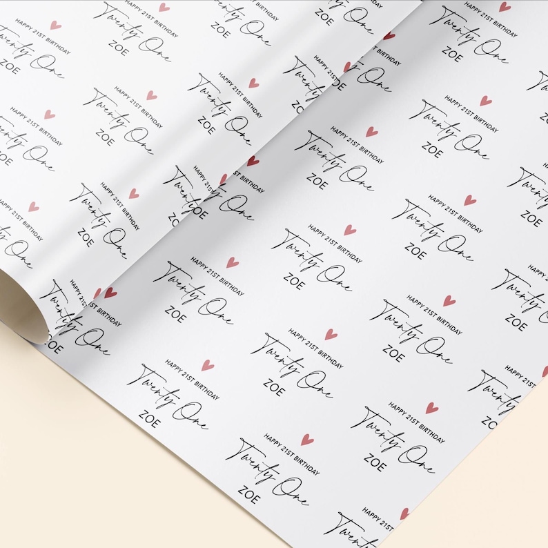 Op de afbeelding: Wit inpakpapier met een herhalend patroon van roze harten en de tekst "Happy 21st Birthday Twenty One Zoe" in zwarte cursieve letters.