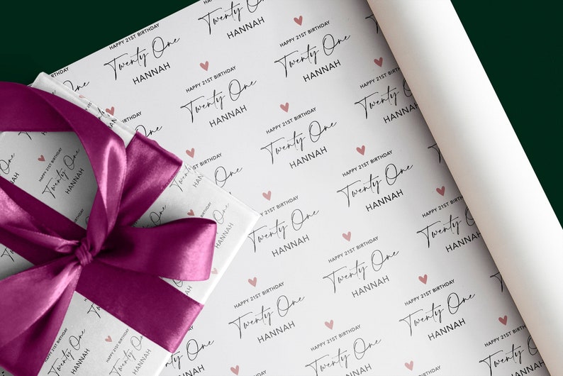 Op de afbeelding: Wit cadeaupapier met een herhalend patroon van roze harten en de tekst "Happy 21st Birthday Twenty One Hannah".