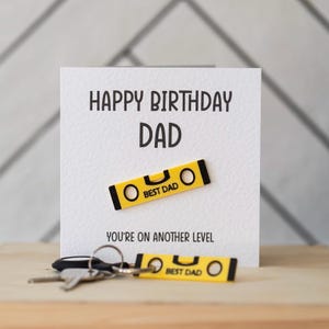 May include: A white card with the text "Happy Birthday Dad" and a yellow level with the text "Best Dad" on it. The card also has the text "You're on another level".