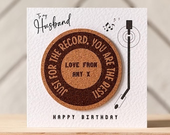 May include: A birthday card with a cork record design. The card reads "To my Husband" and "Just for the record, you are the best! Love from Any X. Happy Birthday". A black record player arm and musical notes are also featured.