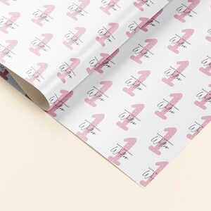 K&ouml;nnte beinhalten: Rosa-wei&szlig;es Geschenkpapier mit einem sich wiederholenden Muster der Zahl eins mit den Worten "Happy Birthday Willow" darauf.